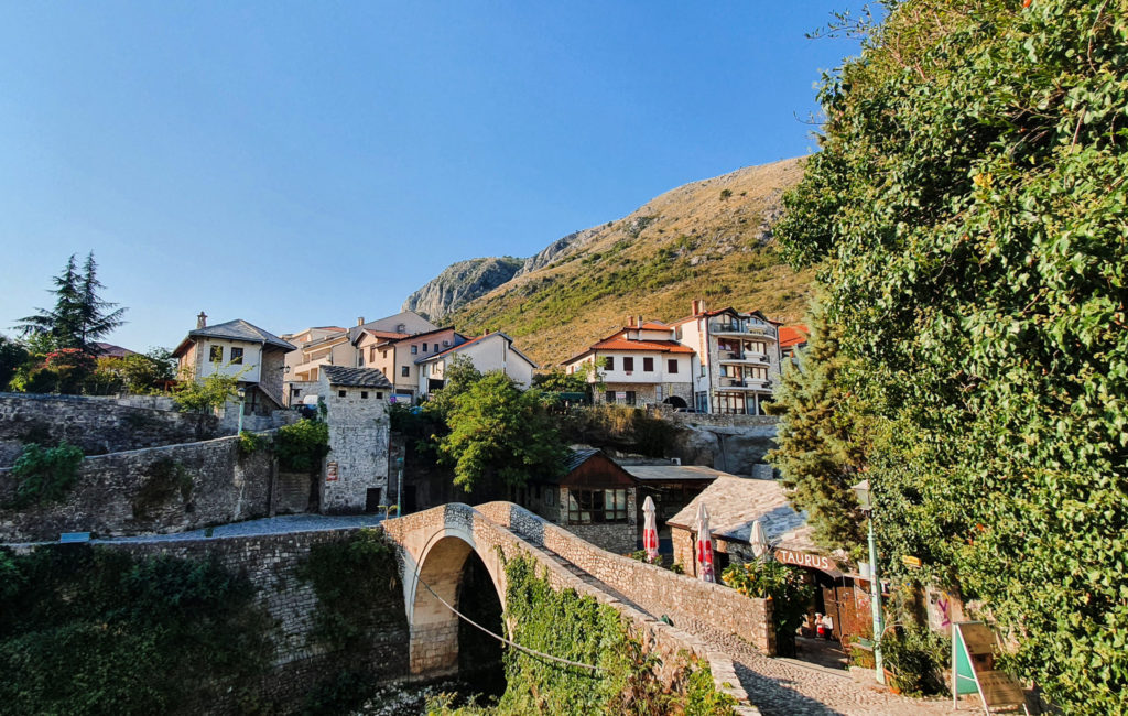 The crooked bridge in Mostar, a smaller version of Stari Most, surrounded by trees and houses