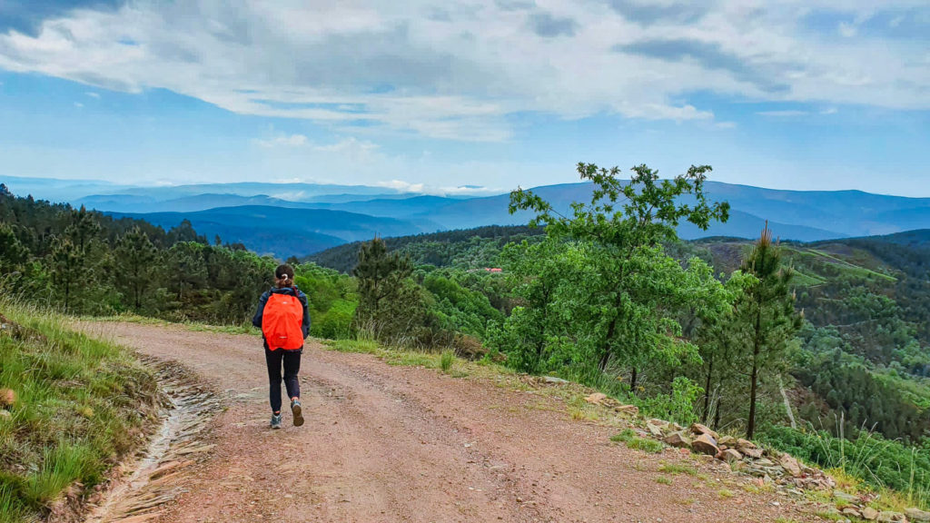 Woman with a backpack walking on a dirt road overlooking tree-covered hills