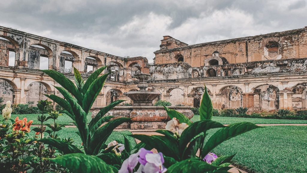 Courtyard at Templo de Santa Clara, with ruins of colonial arches, an array of plants and flowers in the foreground