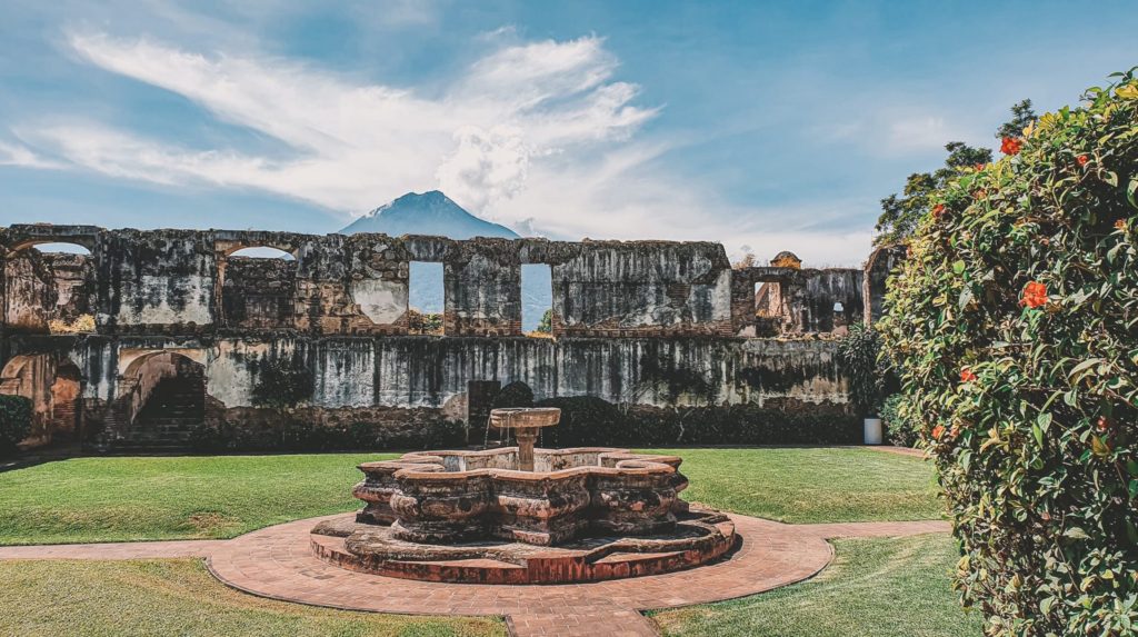 Stone fountain in a courtyard surrounded by colonial ruins, a volcano in the background, Antigua Guatemala