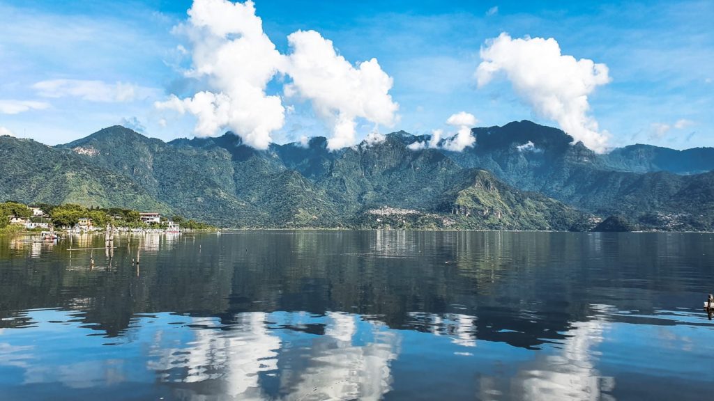 Lake Atitlán with the surrounding mountains and the white clouds mirrored on the calm lake's surface
