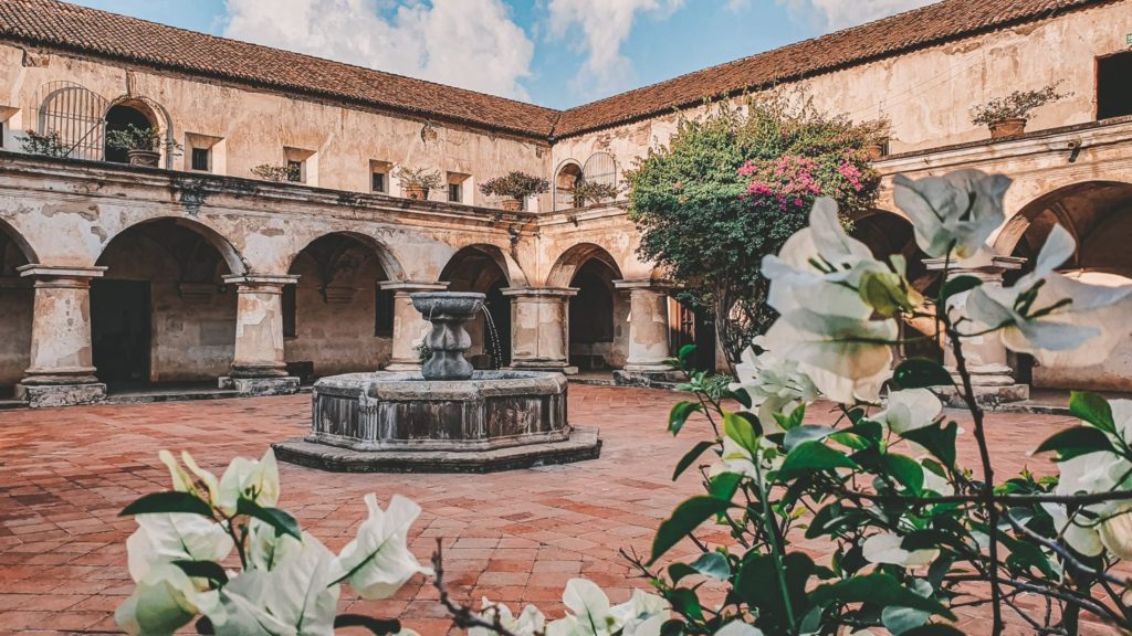Courtyard of a colonial buildig with a fountain in its center, white flowers framing it - Convento Las Capuchinas