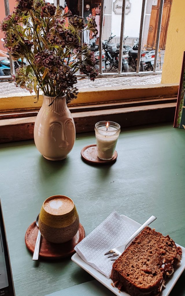 Cappuccino and Banana Bread on a table next to a vase with flowers and a candle at Alegría Café