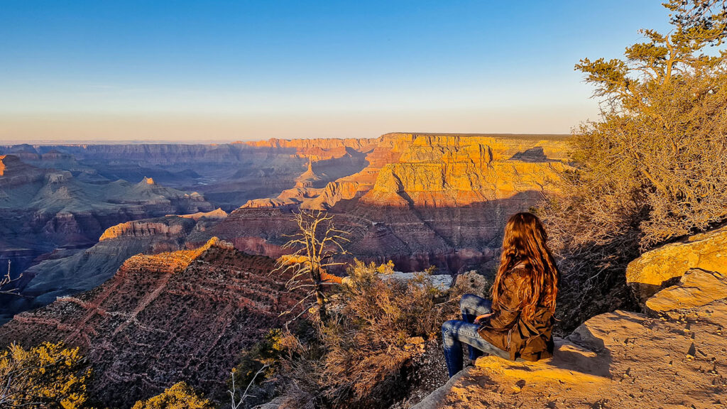 Grand Canyon, US Woman sitting on the edge of the Grand canyon at sunset, back to the camera