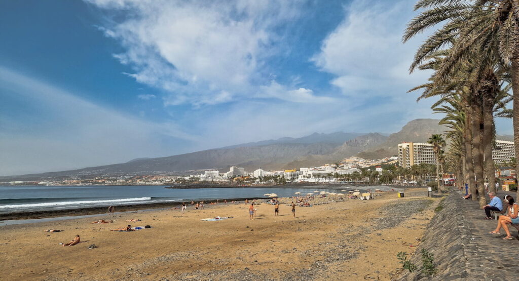 Playa de Las Americas Wide beach with a few people, a promenade lined with palm trees, and mountains in the background, Playa de Las Americas