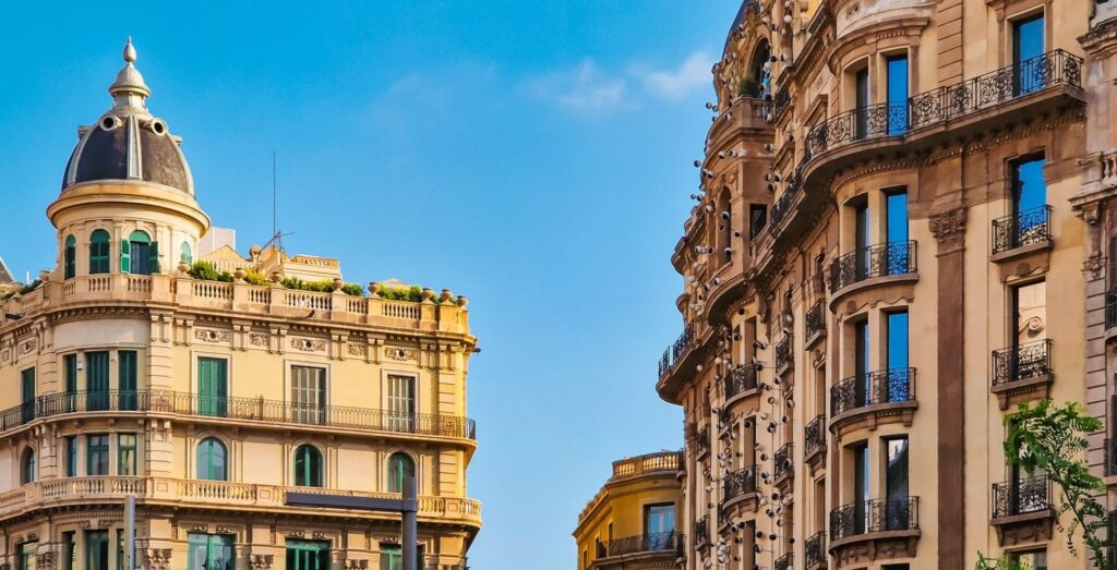 Two ornate European-style apartment buildings with decorative balconies against a clear blue sky - Barcelona, Spain
