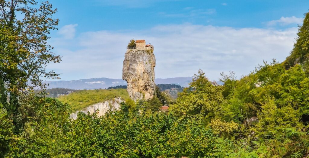 Stone pillar with a monastery on top durrounded by greenery, Georgia