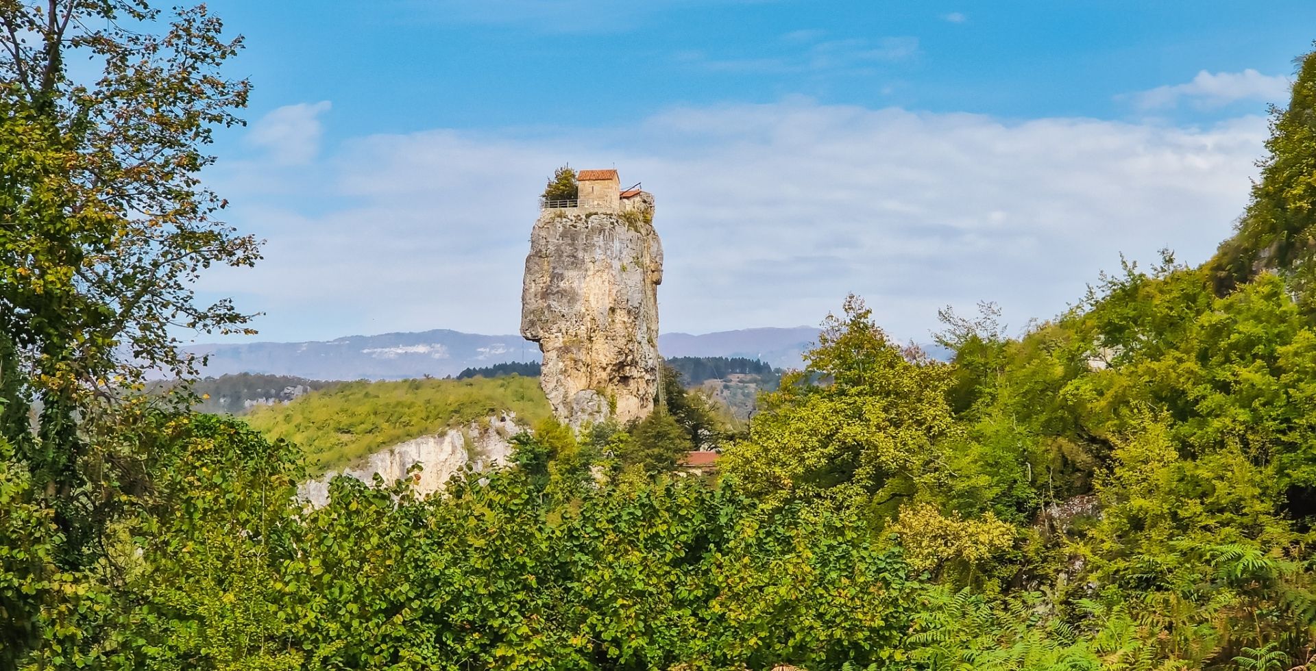 Stone pillar with a monastery on top durrounded by greenery, Georgia