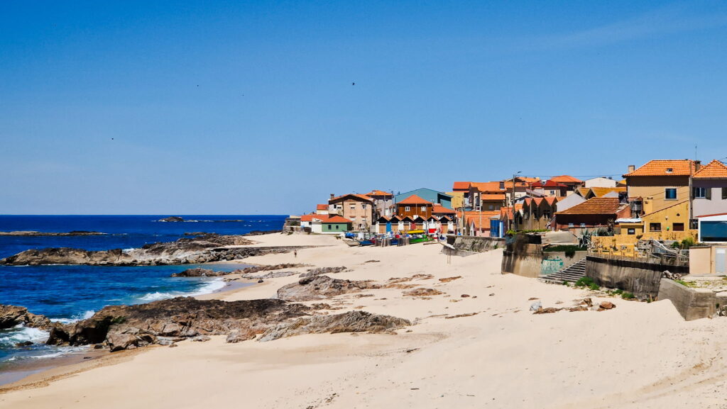 Camino Portugués - Day 1 Coastal town on a sandy beach with colorful houses along the shore and rocky foreground under a clear blue sky