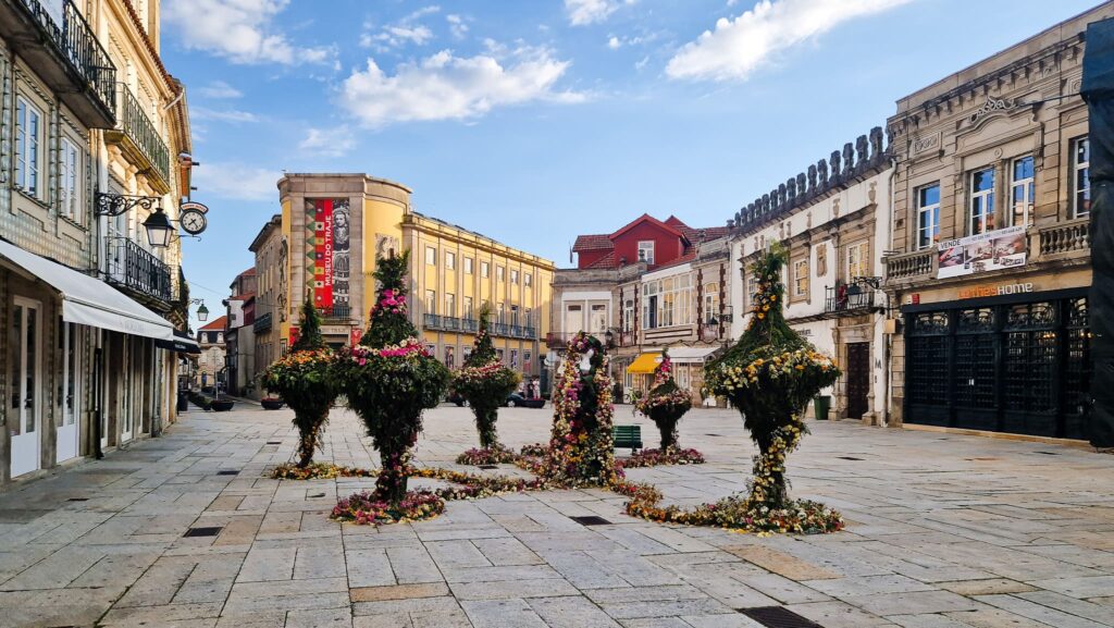 Viana do Castelo Center European town square with ornate historic buildings and flower-covered sculptures arranged in a circular display against a blue sky.