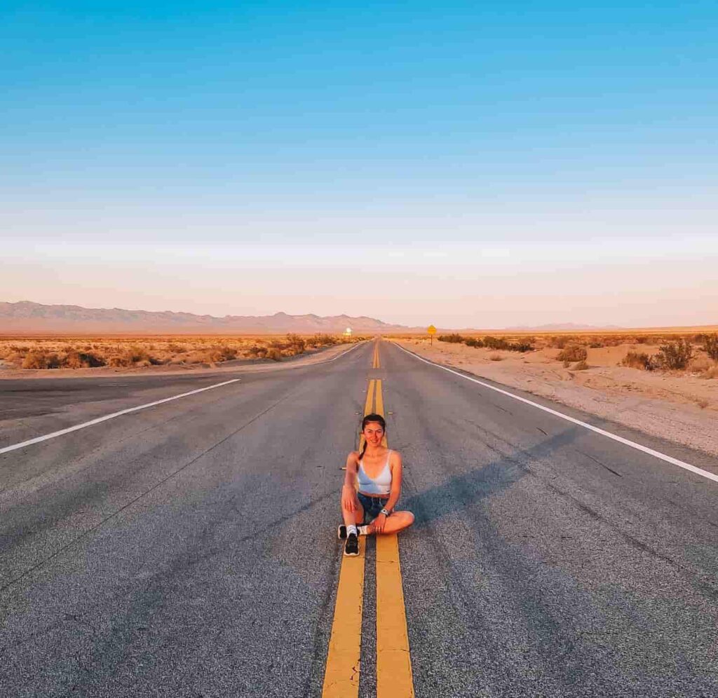 Rox in California Woman sitting in the middle of an empty road in a desert-like landscape in the United States.