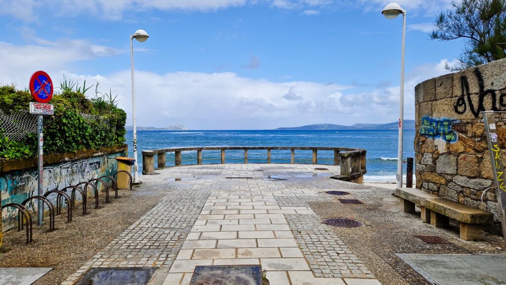 Camino Portugués - Day 7 Promenade by the sea with a stone path, graffiti walls, bike racks, and lamps leading to the ocean.