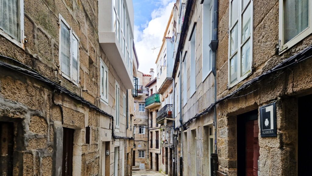 Camino Portugués - Vigo Narrow stone alleyway in the historical center of Vigo, Spain, with tall buildings, balconies, and laundry hanging between them.