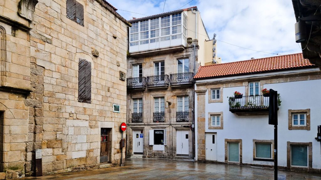 Vigo, Camino Portugués Narrow European street with stone buildings, iron balconies, and a small hostel sign at street level.