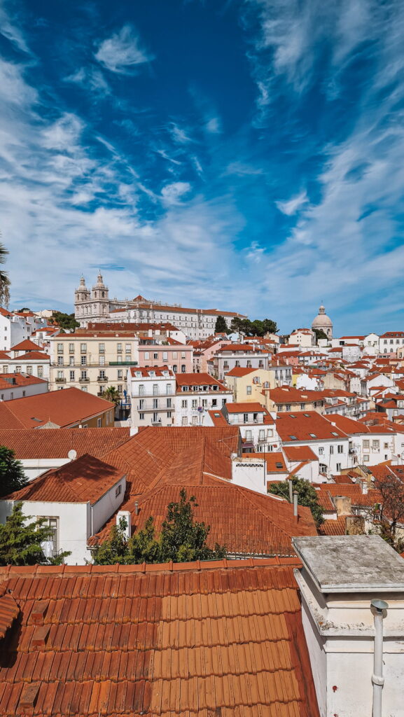 Lisbon, Portugal Lisbon, Portugal: cityscape with terracotta rooftops and pastel buildings beneath a bright blue sky; a domed church sits on the hill.