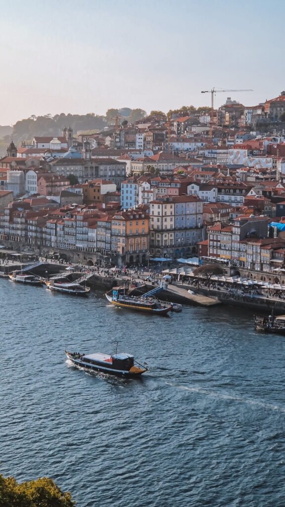 Porto, Portugal The colorful waterfront Porto, with red-roofed buildings along the quay and several boats on the blue water. Site: waterfront cityscape with pastel houses and a busy promenade by the harbor. Portugal travel guides