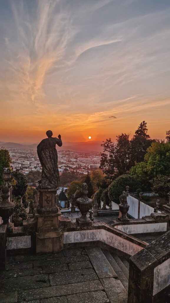 Braga, Portugal Statue in a cloaked figure atop a stone terrace overlooking a city at sunset, with ornamental balustrades and trees in the foreground, Braga, Portugal travel destinations
