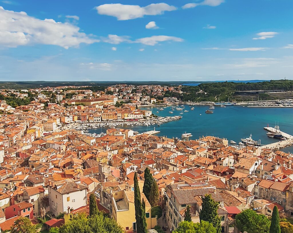 Rovinj day trip A coastal town with orange-tiled roofs and a busy marina under a blue sky, viewed from above.