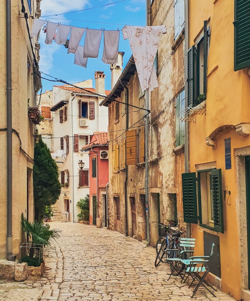 Rovinj Old Town street Narrow sunlit cobblestone street in a European town, colorful stucco buildings, laundry hanging between walls.
