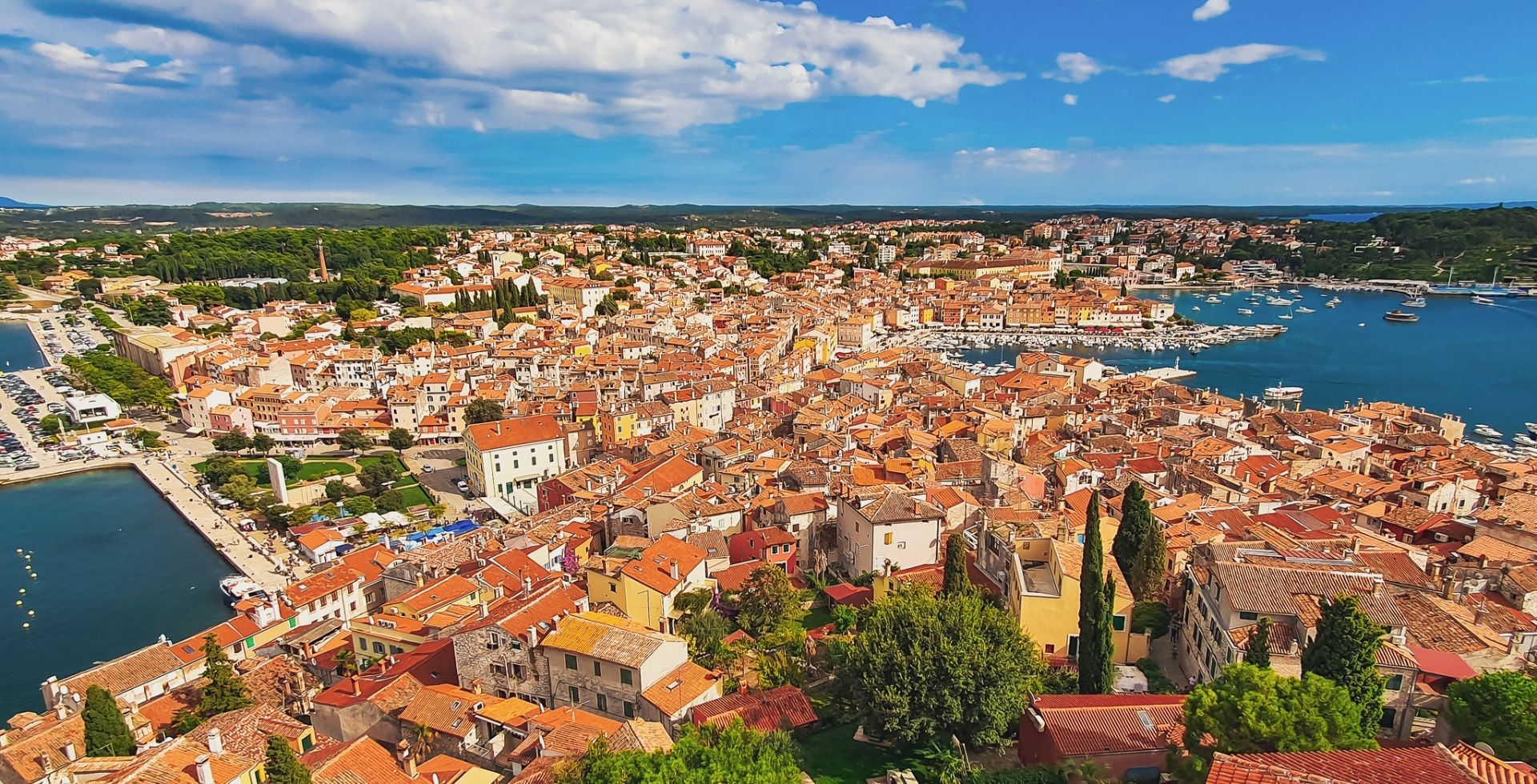 Aerial view of a Mediterranean coastal town with terracotta roofs and a busy harbor filled with boats.