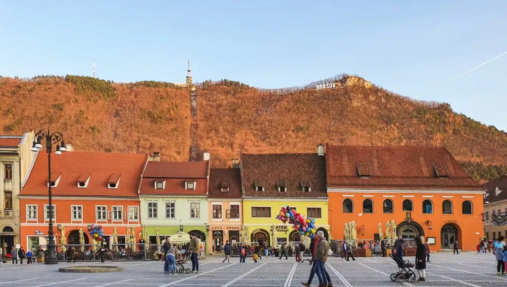 Piata Sfatului- Autumn Square surrounded by colorful medieval buildings with a fall foliage-covered mountain at the back, Brasov, Romania